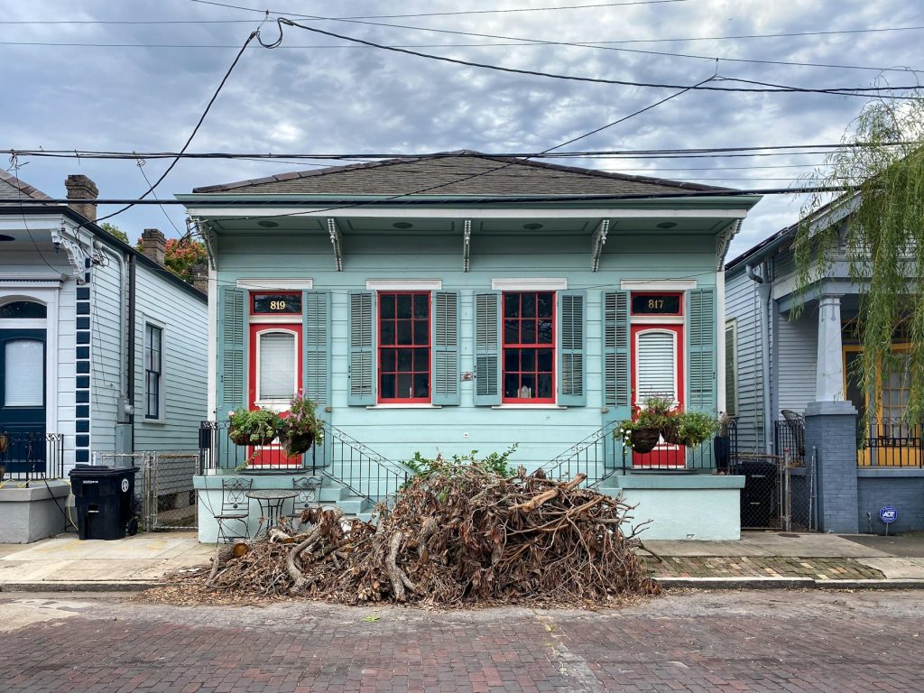 Shotgun house with storm debris piled at the curb