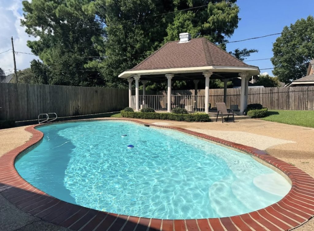Clear kidney-shaped pool with brick coping and a backyard gazebo