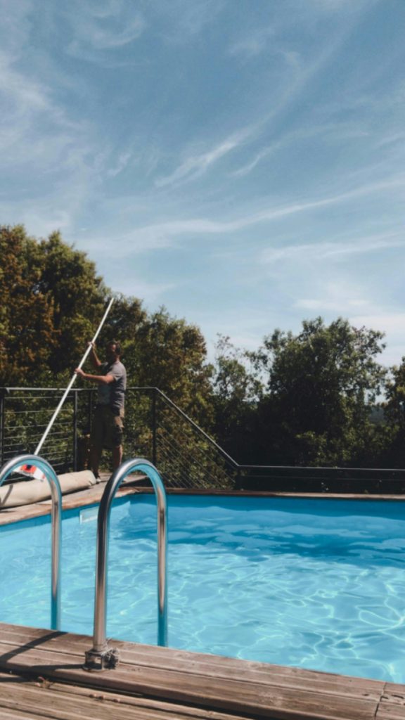 Pool cleaner working with a telescopic pole beside a swimming pool