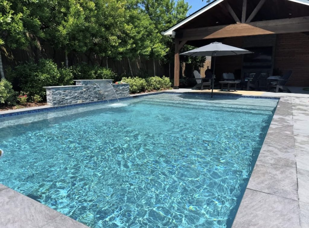 Rectangular pool with stone water feature beside a covered patio