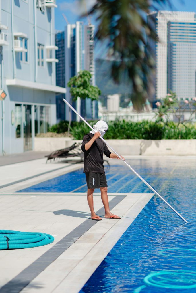 Technician cleaning a residential pool with a telescopic pole